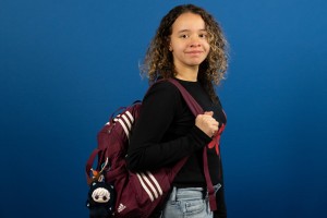 Female student holding their backpack against a blue background