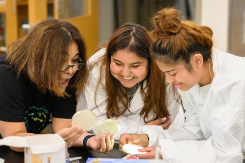 Students with a professor in a science lab holding a petri dish.