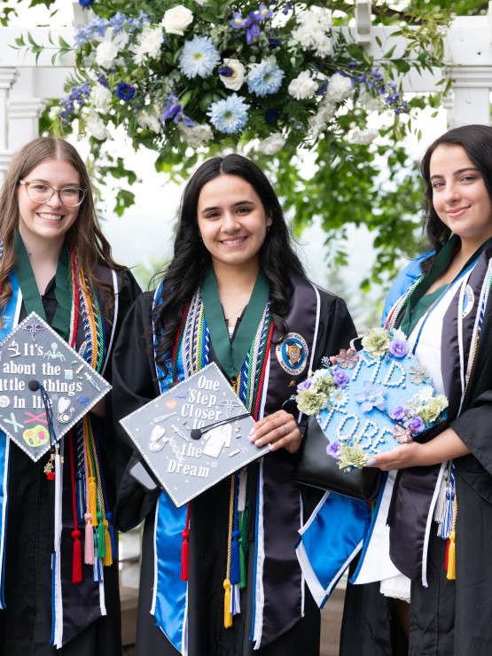 Three students standing together holding their decorated graduation caps.