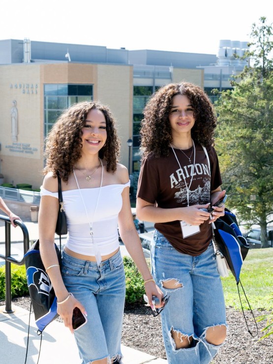Mount students walking up the stairs waving at the camera with Aquinas Hall behind them.
