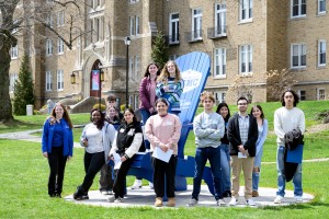 Group of students standing around and on a large Adirondack chair.
