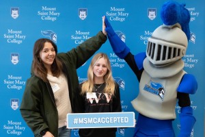 Student giving a high-five to the college's mascot, Mack the Knight, and another student holding a cutout that says "#MSMCAccepted."
