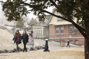 Three students walking on campus as snow is coming down.