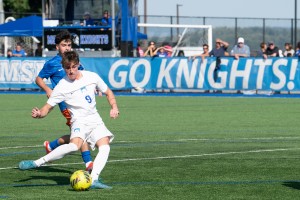 Men's soccer player kicks a soccer ball with spectators cheering them on.
