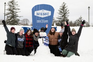 Seven students wearing winter gear and posing with a snowman they made on campus.
