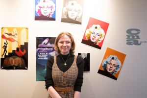 Woman stands in front of art. Liz Linton of Walden, N.Y., a Visual Communication-Graphic Design major at Mount Saint Mary College, stands alongside her work. The display featured a blend of typography and illustration, including her “Marilyn” piece create