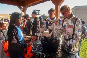 ALT: Mount Saint Mary College students dressed as shiny, silver astronauts give candy to a young student.