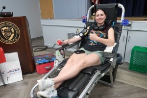 Woman sits in chair, giving blood. 