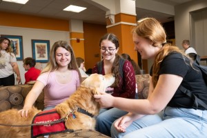 ALT: Three women smile and pet a dog at Mount Saint Mary College.