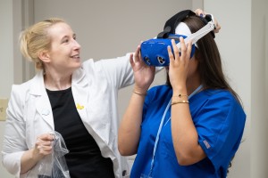 ALT: Professor in a white jacket helps a student experience virtual reality via goggles. 