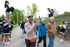 A group of people walking on a path, including cheerleaders performing with pom-poms, surrounded by green trees and a hill at Mount Saint Mary College.