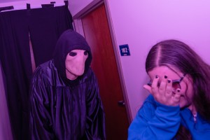ALT: Mount Saint Mary College student covers her face in fright as an alien in a black robe looms overhead. 