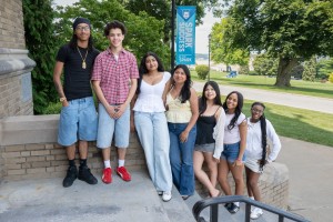 The incoming freshman HEOP class at Mount Saint Mary College finished the Summer Academic Institute on campus earlier this month. ALT: Seven smiling college students standing together along an outdoor campus staircase next to a blue banner reading "S