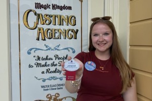 ALT: A woman stands to the left, smiling, as Micky Mouse stands to the right, wearing his red robe and blue hat from Fantasia. 