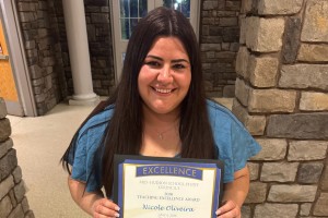 ALT: Woman in a dress holds up a certificate.