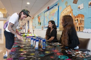 Mount Saint Mary College students enjoy the Hispanic Heritage Month celebration held recently in the Aquinas Hall Atrium. ALT: Students sit at a festively decorated desk, while a man chooses a snack.