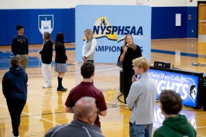 Woman has a microphone. She is in a gym, speaking to student-athletes at Mount Saint mary College. 