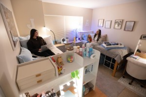 Look inside a dorm room in Sakac Hall. Two students are sitting on their beds with the walls decorated.