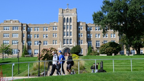 Three students walking on campus with the Dominican Center behind them.