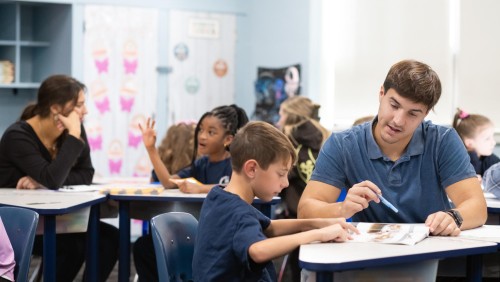 Image of a teacher working with a group of students on the floor.
