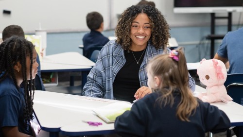Students with younger children teaching in a classroom.