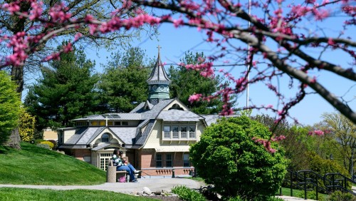 Springtime scenic on campus with Whittaker Hall and students sitting on a bench.