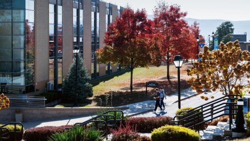 Photo of students walking on a sidewalk during the fall with red colored leaves.