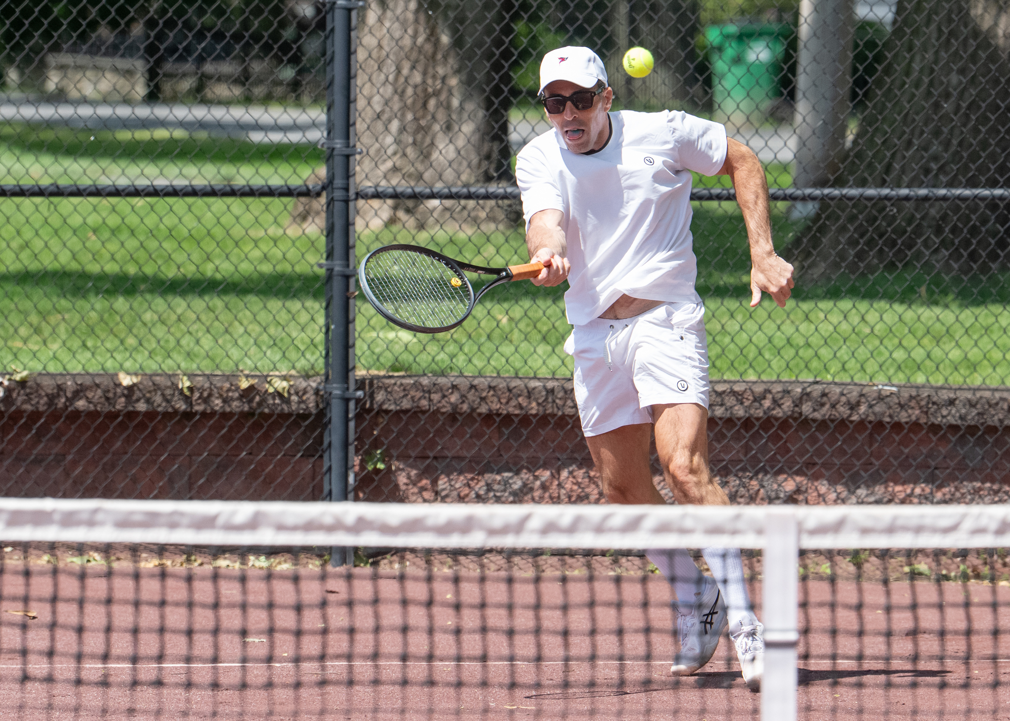 A man in white sportswear prepares to hit a tennis ball with his racket on an outdoor tennis court.