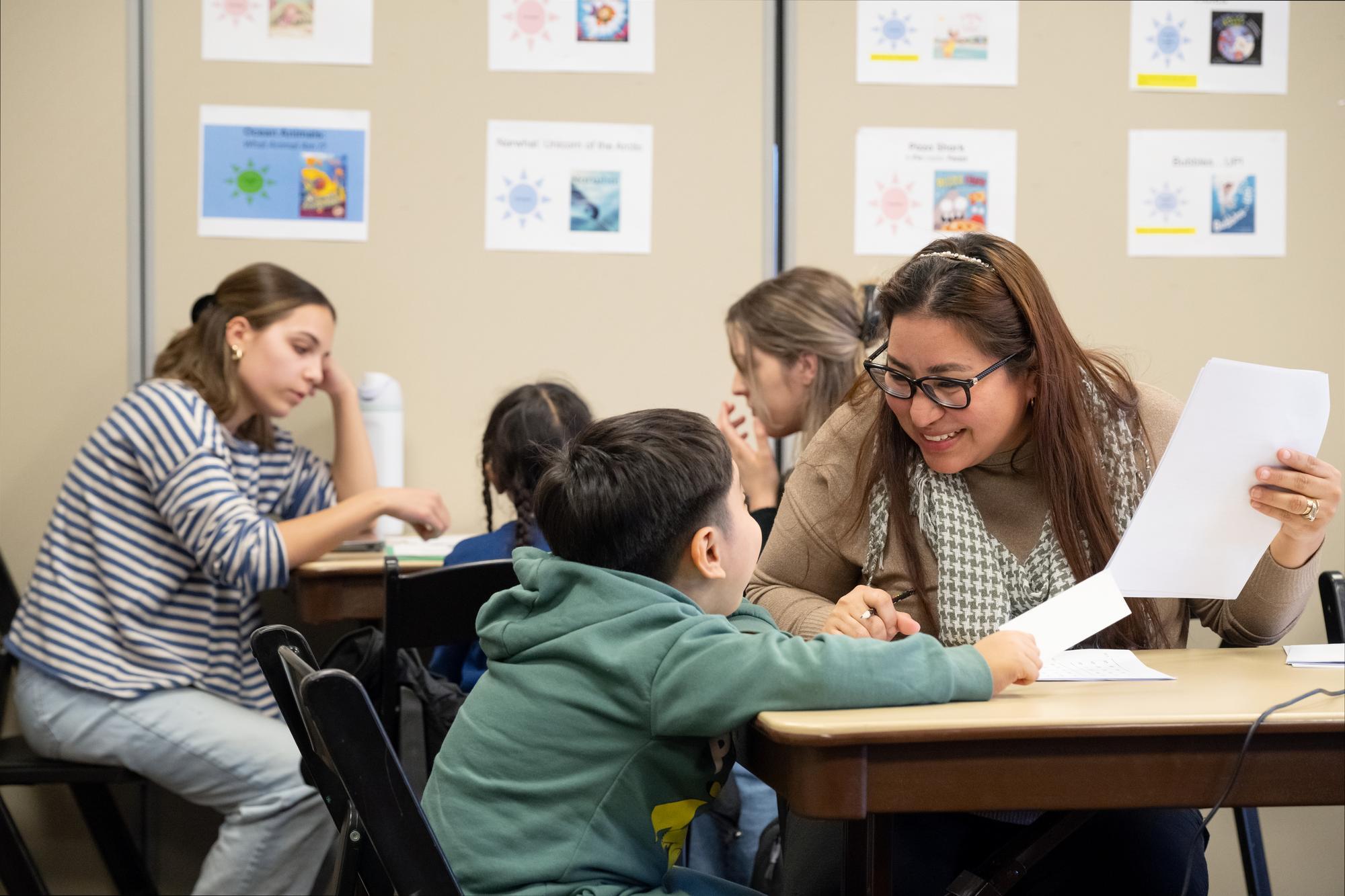 Teacher working with a student in a classroom setting. The teacher is smiling.