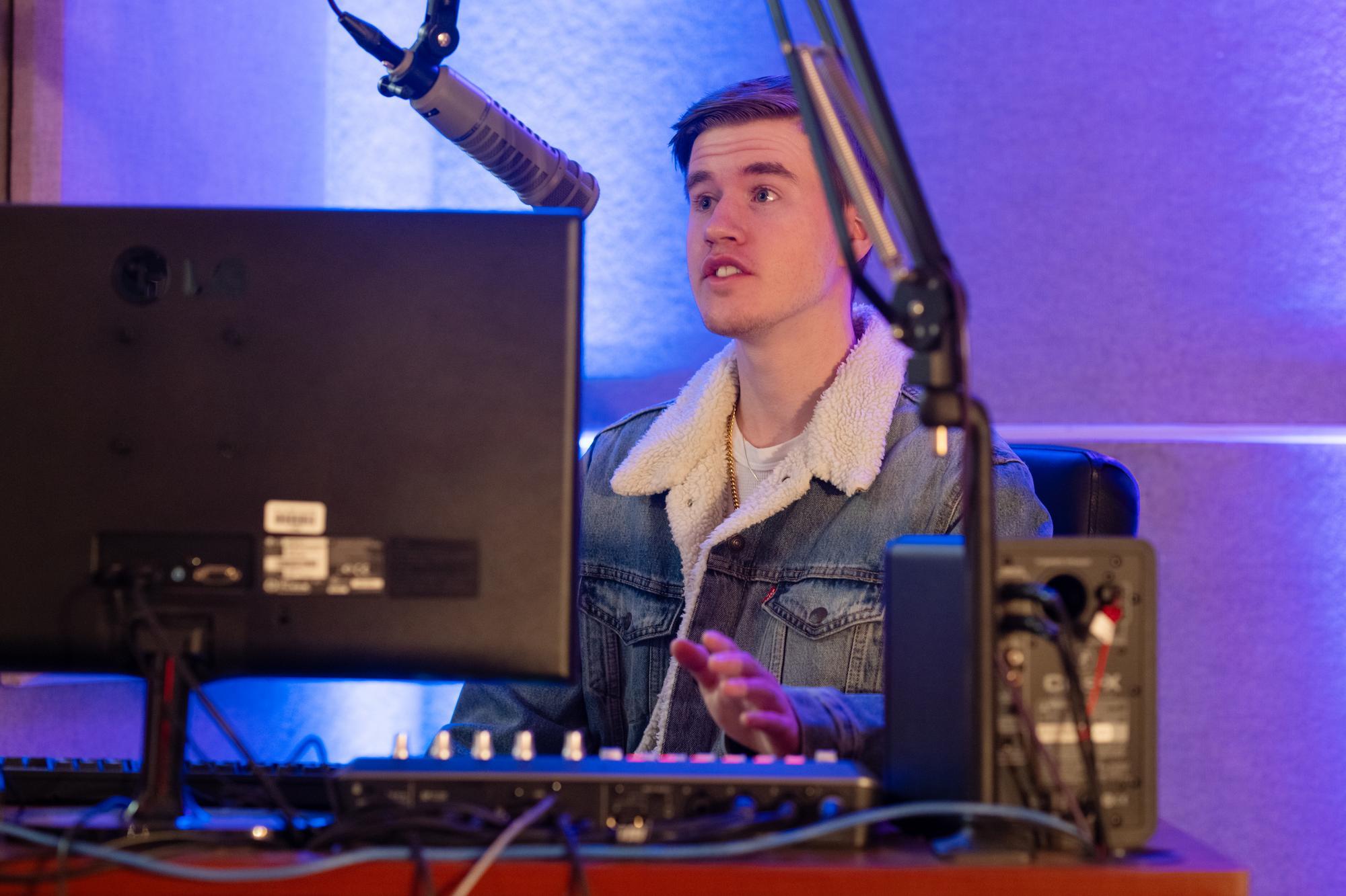 Student speaking into a microphone in front of a computer in the radio station.
