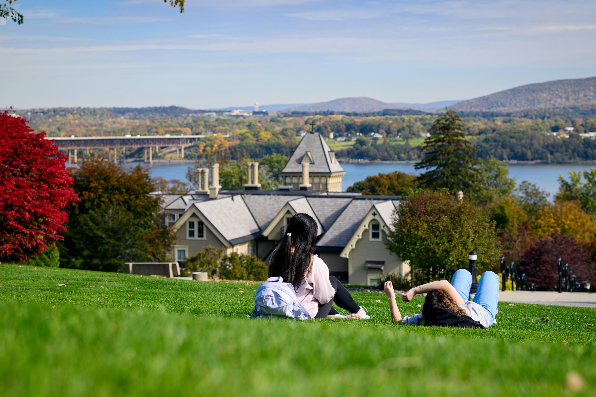 Two students relaxing on the hill overlooking the Villa and Hudson River during fall.