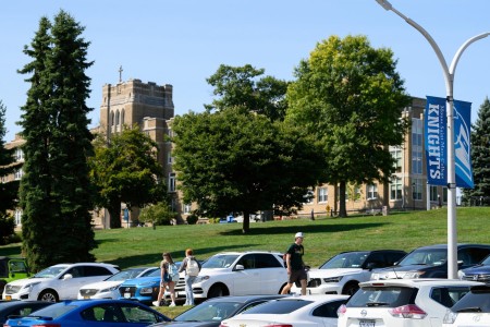 Parking lot with cars looking up at the Dominican Center with students.