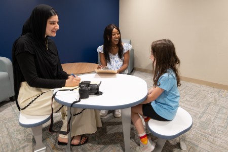 Two students sitting at a table with a young child.
