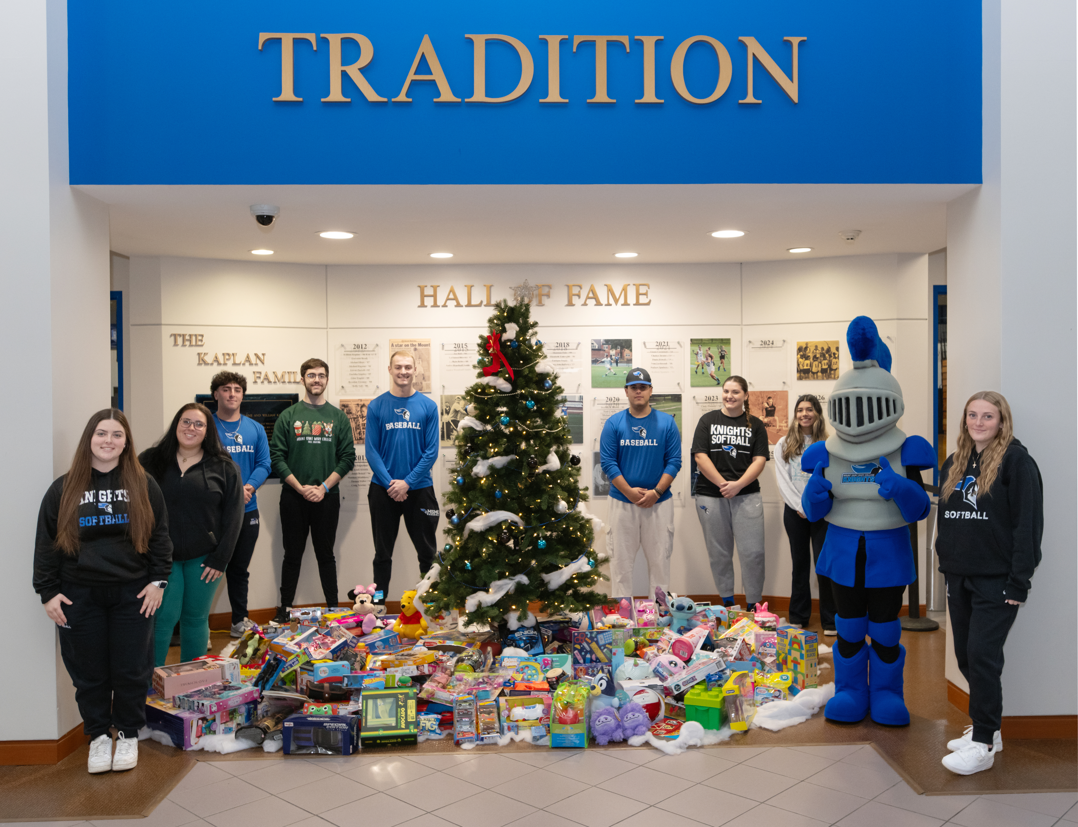 Students inside the Kaplan Gym lobby in front of a Christmas tree and toys for the annual Toy Drive.